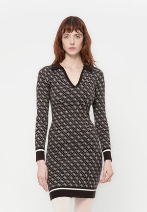 Donna che indossa un abito lungo con maniche aderenti di colore marrone, con un motivo a diamante bianco, colletto a V e bordi bianchi ai polsini e all'orlo, su uno sfondo bianco.