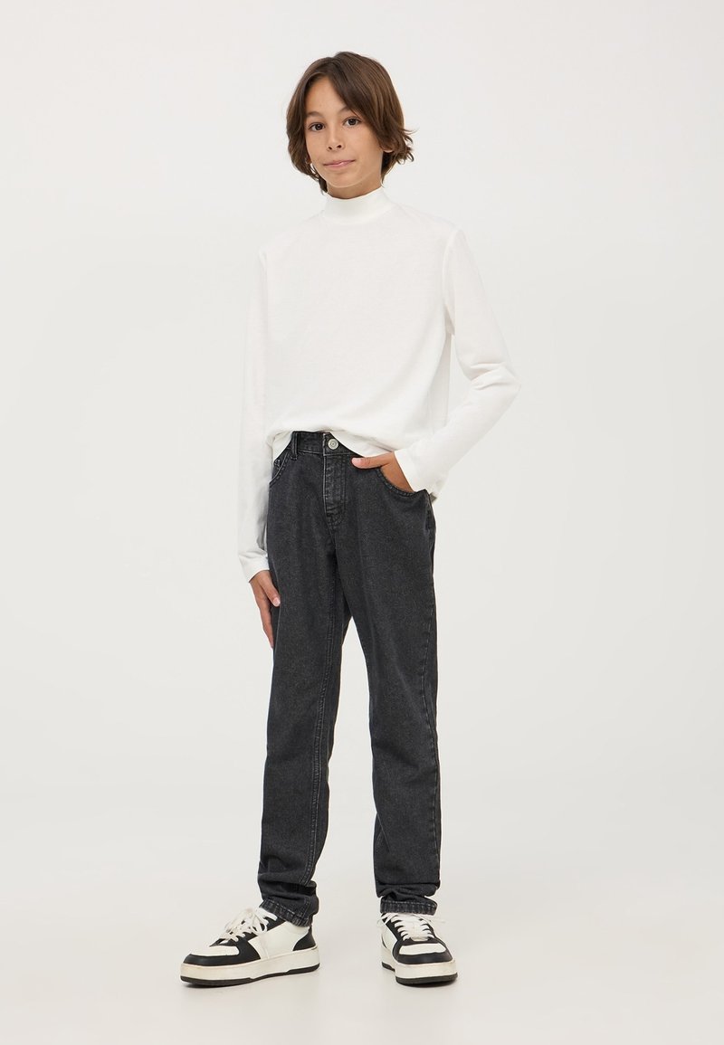 Maglietta bianca a maniche lunghe con colletto a dolcevita, jeans grigi scuri a gamba affusolata, scarpe da ginnastica nere e bianche, look informale, design semplice, texture del tessuto visibili.