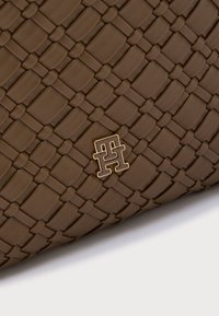 Pruun kootud nahast kott, millel on kuldse tooniga logoaksent. Tekstuurse pinnaga, millel on ühtlane põimitud ribade muster.