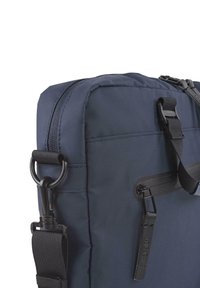 Bolsa de nailon azul oscuro con una textura suave, que cuenta con un cierre de cremallera, correa ajustable y detalles en negro.