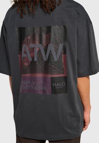 Osoba nosząca ciemnoszary, oversize'owy t-shirt z geometrycznym motywem góry oraz napisami „ATW”, „OFF DUTY GEAR” i „HALO” na plecach.