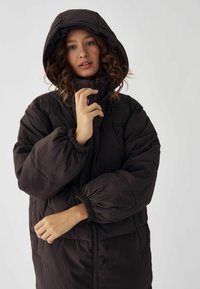Melns, kapuces puf jacket ar šūnu tekstūru, elastīgām aprocēm un priekšējo rāvējslēdzēju. Ievērojams augsts apkakle un sānu kabatas.
