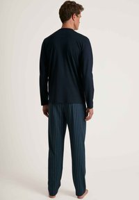 Haut à manches longues bleu marine avec col rond, associé à un pantalon bleu marine à motifs avec de petits points colorés et des jambes droites.