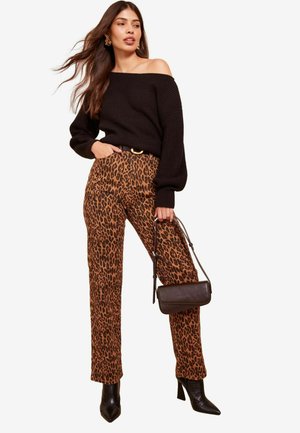 Schwarzer schulterfreier, gerippter Pullover, kombiniert mit einer hoch taillierten Hose im Leopardenmuster. Das Model hält eine kleine schwarze Handtasche und trägt schwarze Stiefeletten mit Absatz.