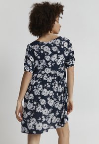 Laivastonsininen mekko, jossa on valkoinen kukkakuosi, lyhyet puffhihat ja kierretty vyötärö. Pehmeä kangas, rento malli ja liehuva helma.