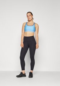Blå sports BH med sort trim, sorte høytalende tights, og svarte treningssko. Formtilpasset design, glatt tekstur, ingen synlige mønstre.