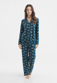 Pyjama-Set mit einem blauen Stoff und einem Dackelmuster. Das Oberteil hat einen Hemdkragen und die Hose ist locker sitzend mit einem elastischen Bund.