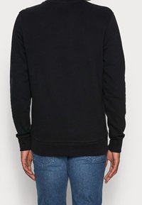 Felpa nera a maniche lunghe, tessuto strutturato, collo rotondo e fondo a coste, vista da dietro, abbinata a jeans blu.