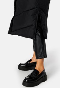 Sort puffetjakke med quiltet design, med sidelukning og trykknaplukning. Sammen med sorte læder tapered bukser og platform loafers.