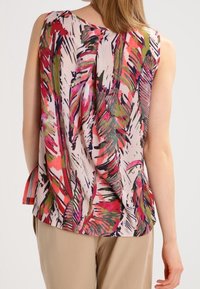 Bezrukávový, lehký top s barevným tropickým listovým vzorem v růžové, zelené a černé na světlém pozadí, s uvolněným střihem.