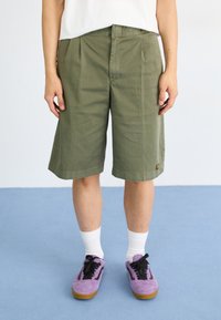 Olive green cargo shorts with pleats, made from cotton. Paired with purple sneakers and white crew socks. Simple design with side pockets.