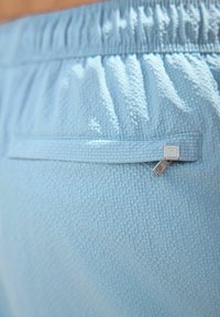 Shorts de culoare albastru deschis, realizate dintr-un material texturat, cu un centru elastic la talie și o mică buzunar cu fermoar, detaliat cu un element metalic.