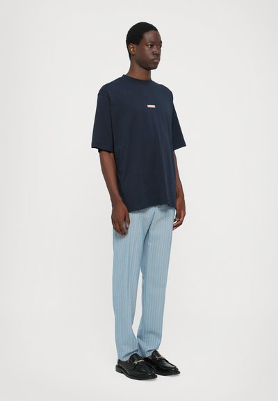 Mörkblå bomull t-shirt med en liten röd logotyp, i kombination med ljusblå randiga byxor och svarta loafers.