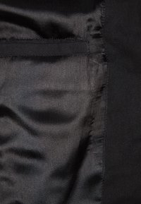 Černá tkanina s hladkou texturou, vybavená tmavou podšívkou a švy. Povrch je jednotný s minimem viditelných detailů nebo vzorů.