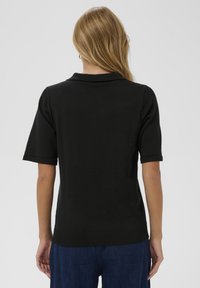 Camiseta polo negra de manga corta con cuello y dobladillo de canalé, que presenta una textura suave, un diseño ajustado y sin adornos visibles.