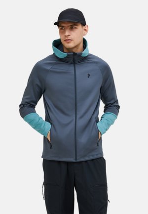 Skræddersyet grå jakke med en teal akcent på ærmerne. Har en høj krave, lynlåslukning og sidelommer. Designet til udendørs aktiviteter.