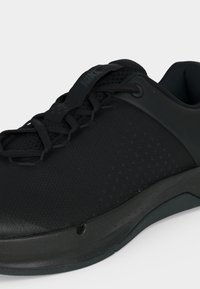 Μαύρο αθλητικό παπούτσι Nike με επάνω μέρος από δίχτυ, δέσιμο με κορδόνια μπροστά και υφασμένο πέλμα, εμφανιζόμενο από πλάγια γωνία σε απλό φόντο.