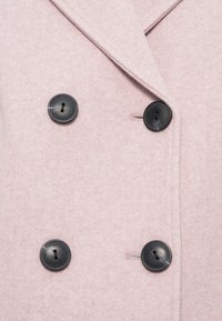 Manteau en laine rose clair avec quatre grands boutons ronds noirs et un large col à revers.