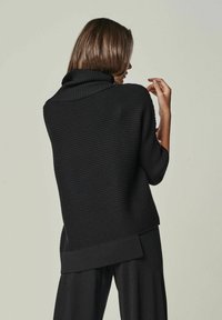 Schwarzer gerippter Pullover mit hohem Rollkragen, kurzen Ärmeln und lockerer Passform. Auffällige Details sind ein längerer hinterer Saum und der strukturierte Stoff.