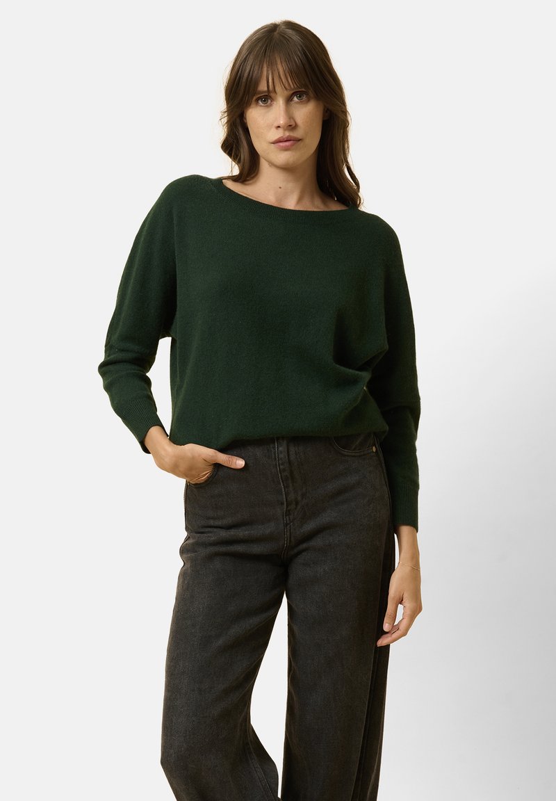 Groene gebreide trui met een brede halslijn en lange mouwen, gecombineerd met hoog- taille zwarte jeans. Zachte textuur, ontspannen pasvorm.