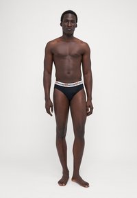 Fekete pamut bikini alsó fehér derékrésszel, amelyen a Moschino logó és a medve minta látható. Normál fazon, extra minták nélkül.