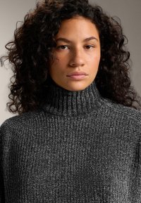 Sivý hrebienkový rolák so štruktúrovaným pletením. Tkanina má jemný lesk a mäkký vzhľad, s vysokým golierom.