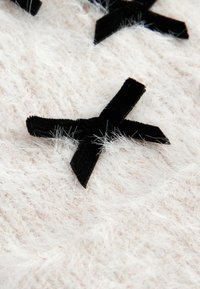 Des rubans en velours noir en forme de croix sur un fond doux, blanc et duveteux. La texture semble floue avec de fines fibres visibles.