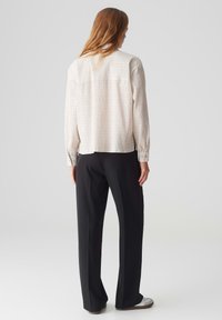 Hell gefärbte, strukturierte Bluse mit langen Ärmeln und geradem Schnitt, kombiniert mit schwarzen Palazzo-Hosen und grauen Slippern.