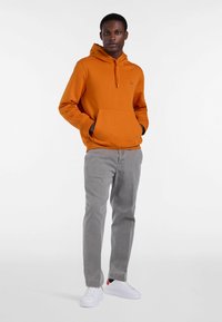 Pomarańczowa bluza z kapturem i kieszenią kangurką, szare spodnie i białe sneakersy. Tekstura jest gładka, materiał wydaje się miękki i casualowy.