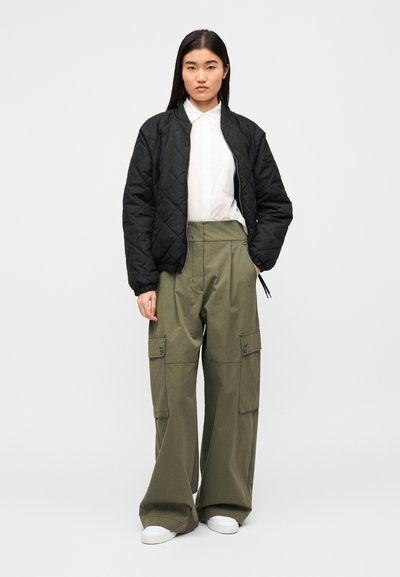 Μαύρο bomber μπουφάν με καπιτονέ υφή πάνω από λευκό πουκάμισο, συνδυασμένο με ψηλόμεσα χακί παντελόνια cargo με μεγάλες τσέπες και φαρδιές παντελόνες.