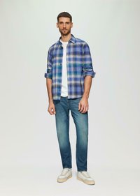 Geruit overhemd in blauwe en groene tinten, dichtgeknoopt, met opgerolde mouwen; gecombineerd met lichtblauwe jeans en witte sneakers. Eenvoudige en casual kleding.