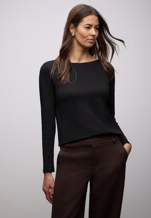Černé tričko s dlouhým rukávem z hladké tkaniny, s kulatým výstřihem a volným střihem. Doplněno o hnědé šité kalhoty.