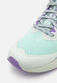 Chaussure de sport avec une tige en maille vert menthe, des accents blancs et une semelle en caoutchouc violette. Présente des détails texturés et des lacets de soutien.