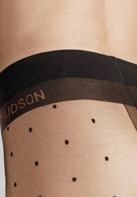 Durchsichtige schwarze Strümpfe bis zum Oberschenkel mit einem schwarzen Band, das mit "HUDSON" geprägt ist, und gepunkteten Mustern am Bein. Glatte Textur.