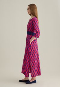 Maxikleid in pink, rot und marineblauem geometrischem Muster, mit einem einfarbigen marineblauen Taillenbund und zwei Seitentaschen. Mit Dreiviertelärmeln.