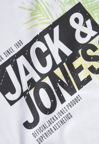 T-shirt bianca con grande tipografia in bianco e nero per "JACK & JONES" e elementi grafici in verde e giallo. Tessuto di cotone morbido.