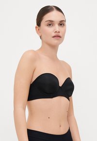 Sort stropløs bh med formede kopper; glat stoffinish og buet bånddesign; minimal syning og ingen synlige hardwaredetaljer.