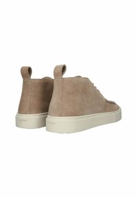 Beżowe zamszowe sneakersy typu high-top z pętlami do wsuwania i białymi gumowymi podeszwami, widoczne z tyłu i lekko pod kątem na bok.