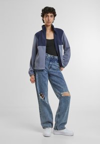 Fleece zip jakke i navy og lys grå, parret med slidte lyse jeans. Hvite sneakers fuldender det afslappede sæt.