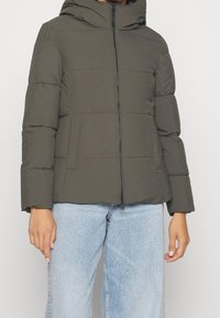 Oliivinvihreä toppatakki hupulla, jossa on etuvetoketju ja sivutaskut, valmistettu sileästä materiaalista.