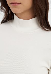 Hvit, ribbestrikket turtleneck genser med en tettsittende design. Glatt tekstur med subtile vertikale linjer som fremhever et rent, minimalistisk utseende.