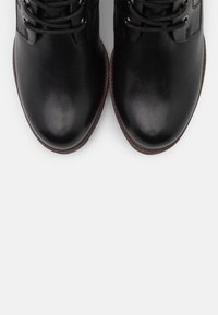 Sorte læderankelstøvler med runde tæer, snørelukning foran og teksturerede detaljer. Brune gummisåler giver holdbarhed og godt greb.