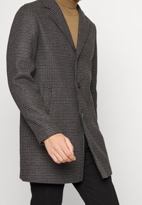 Cappotto grigio a motivo houndstooth con chiusura a due bottoni, rever a punta e tasche laterali, realizzato in tessuto testurizzato. Maniche lisce.