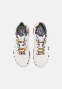 Zapatillas deportivas blancas con acentos de un patrón de zigzag colorido, que presentan un diseño perforado, material suave y cordones decorativos.