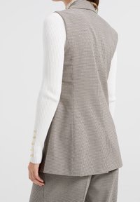 Šedá vesta s pepito vzorem, s límečkem a střih na míru, doplněná bílým žebrovaným tričkem s dlouhým rukávem a zlatými knoflíkovými akcenty.