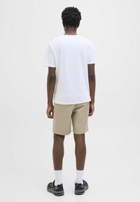 Tricou alb din bumbac cu mânecă scurtă, asortat cu pantaloni scurți bej. Modelul poartă adidași negri și șosete albe, văzut din spate.