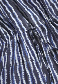 Tissu bleu foncé avec des rayures verticales teintées à la manière tie-dye en blanc et bleu clair, et une taille froncée avec des cordons de serrage assortis.