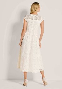 Weißes Spitzenkleid mit floralem Muster, kurzen Ärmel und knielangem Saum. Verfügt über einen verdeckten Reißverschluss hinten und gewellte Kanten.