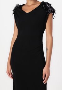 Robe sans manches noire avec un décolleté en V et des détails de franges noires et violettes texturées aux épaules. Tissu lisse, silhouette ajustée.