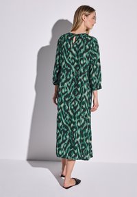 Vihreä ja musta kuviollinen mekko, jossa on avainaukkotakaosa, kolmen neljänneksen hihat ja rento malli, joka ulottuu polven keskikohtaan.